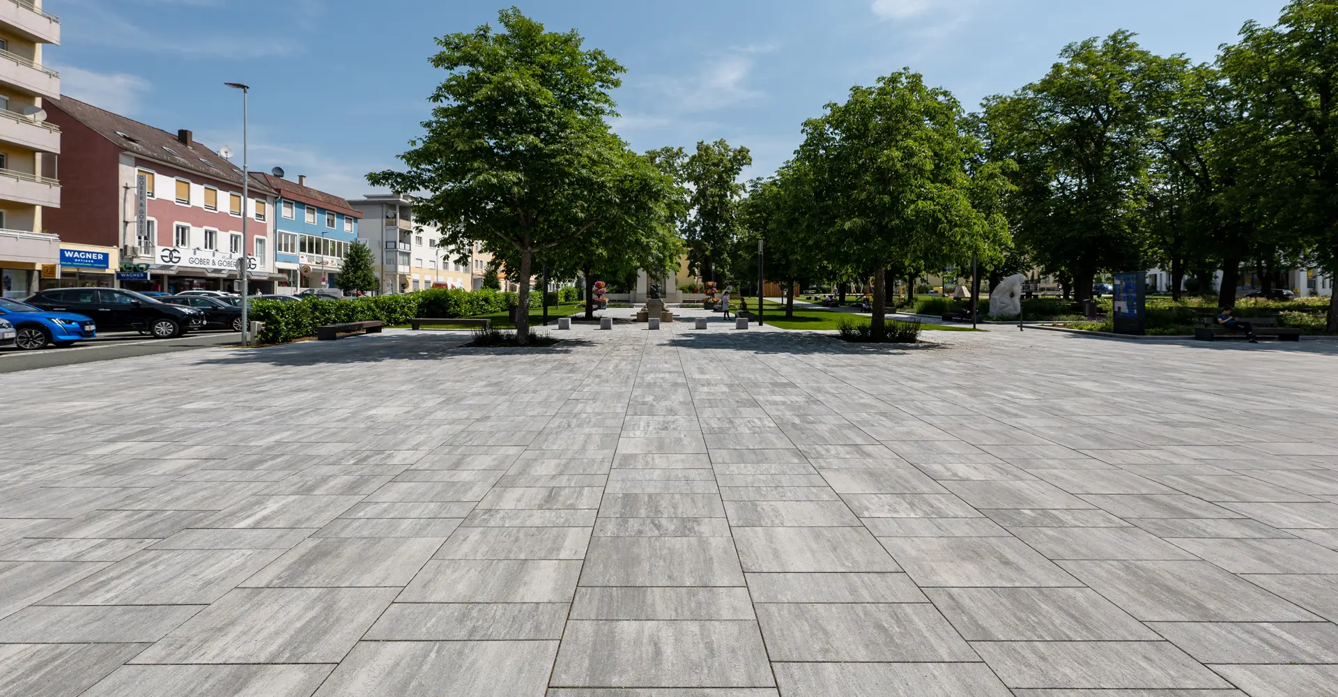 Weitläufige Platzfläche im Stadtgarten Oberwart mit Magnum Platten granitgrau-schattiert zwischen Bäumen, Friedl Steinwerke.