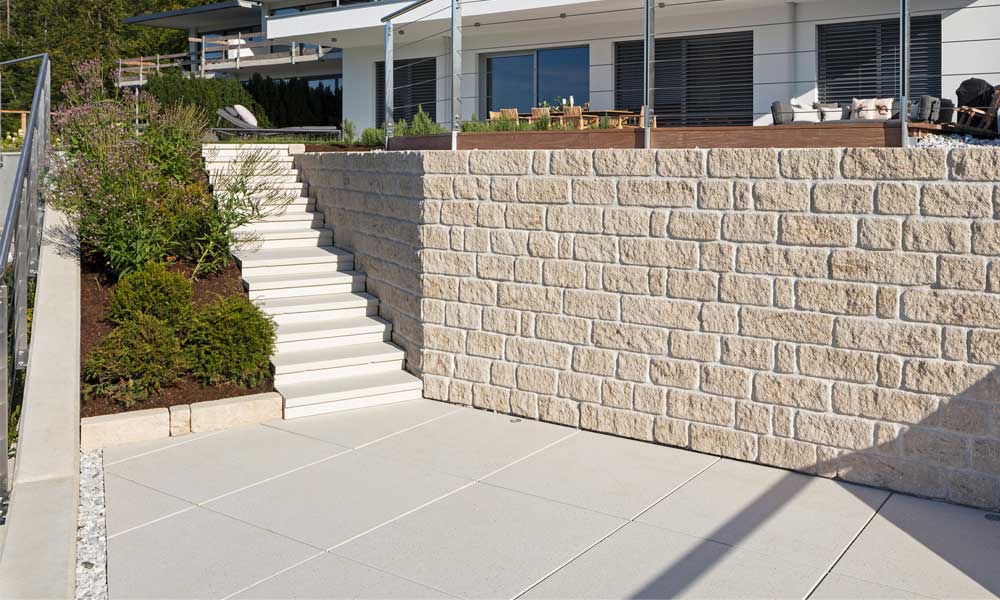 Dots 89,4 x 89,4 x 4,8 cm kreide kombiniert mit Mauerstein Gutshof MB16 bossiert kalkstein-schattiert mit Mörtelfuge vor Betonmauer als Verblendung versetzt