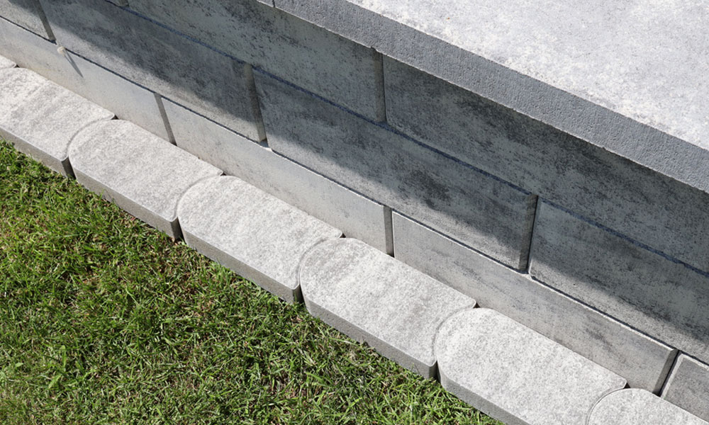 Mähkante granitgrau-schattiert von Friedl Steinwerke als Randeinfassung einer Mauer – funktional und dekorativ im Garten verlegt.
