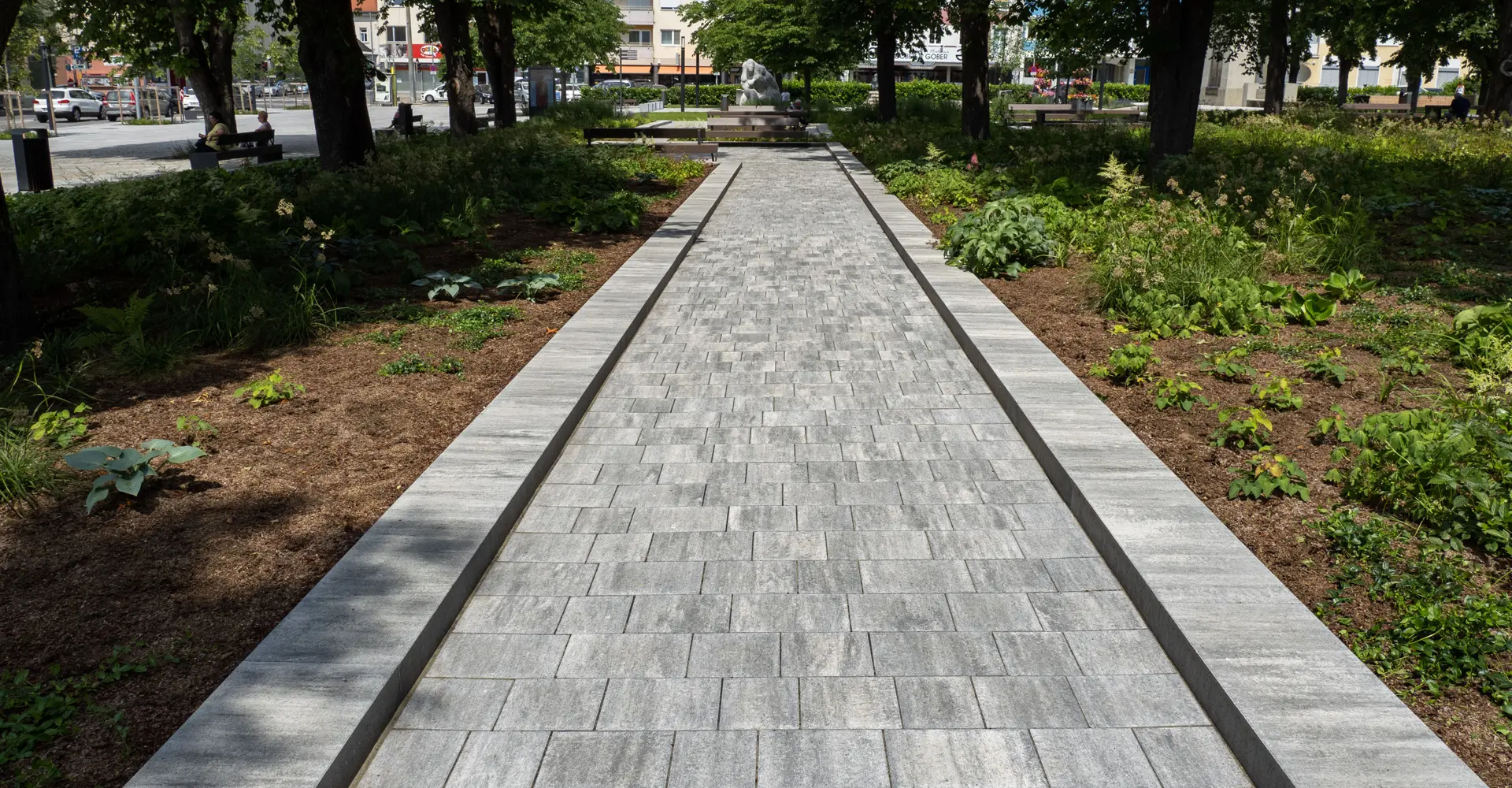 Weg im Stadtgarten Oberwart mit Arret B25 VG4 Kombipflaster granitgrau-schattiert zwischen Beeten und Bäumen, Friedl Steinwerke.